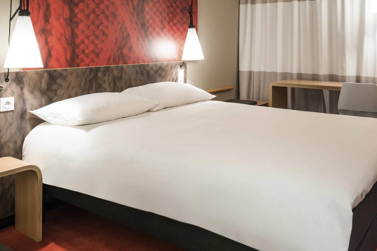 A hotel room with a bed, bedside tables, a desk, and a chair.