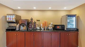 A hotel breakfast area with a coffee machine, a refrigerator, and various food items.