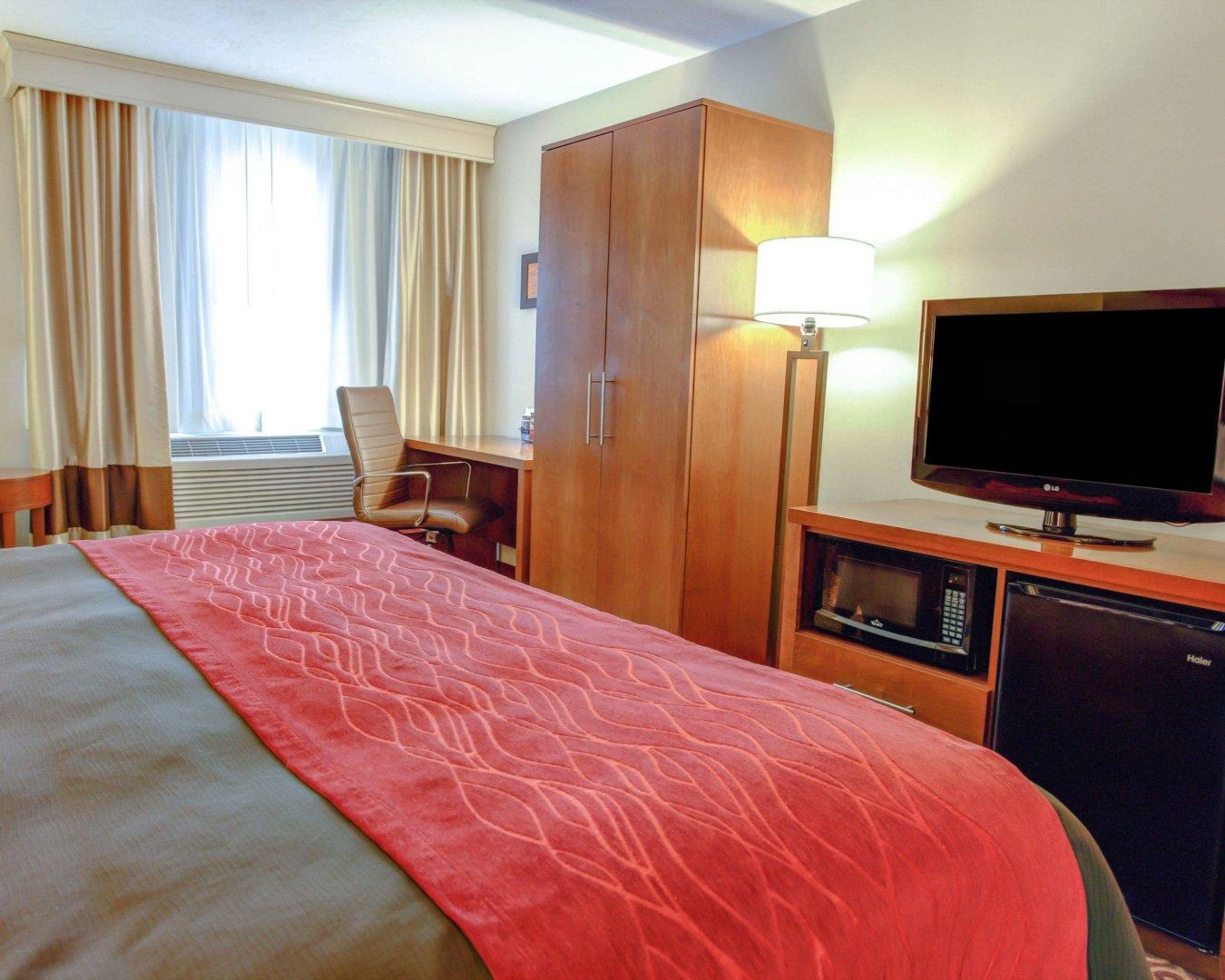 Ein Hotelzimmer mit einem Bett, einem Schreibtisch, einem Fernseher, einer Mikrowelle und einem Schrank.