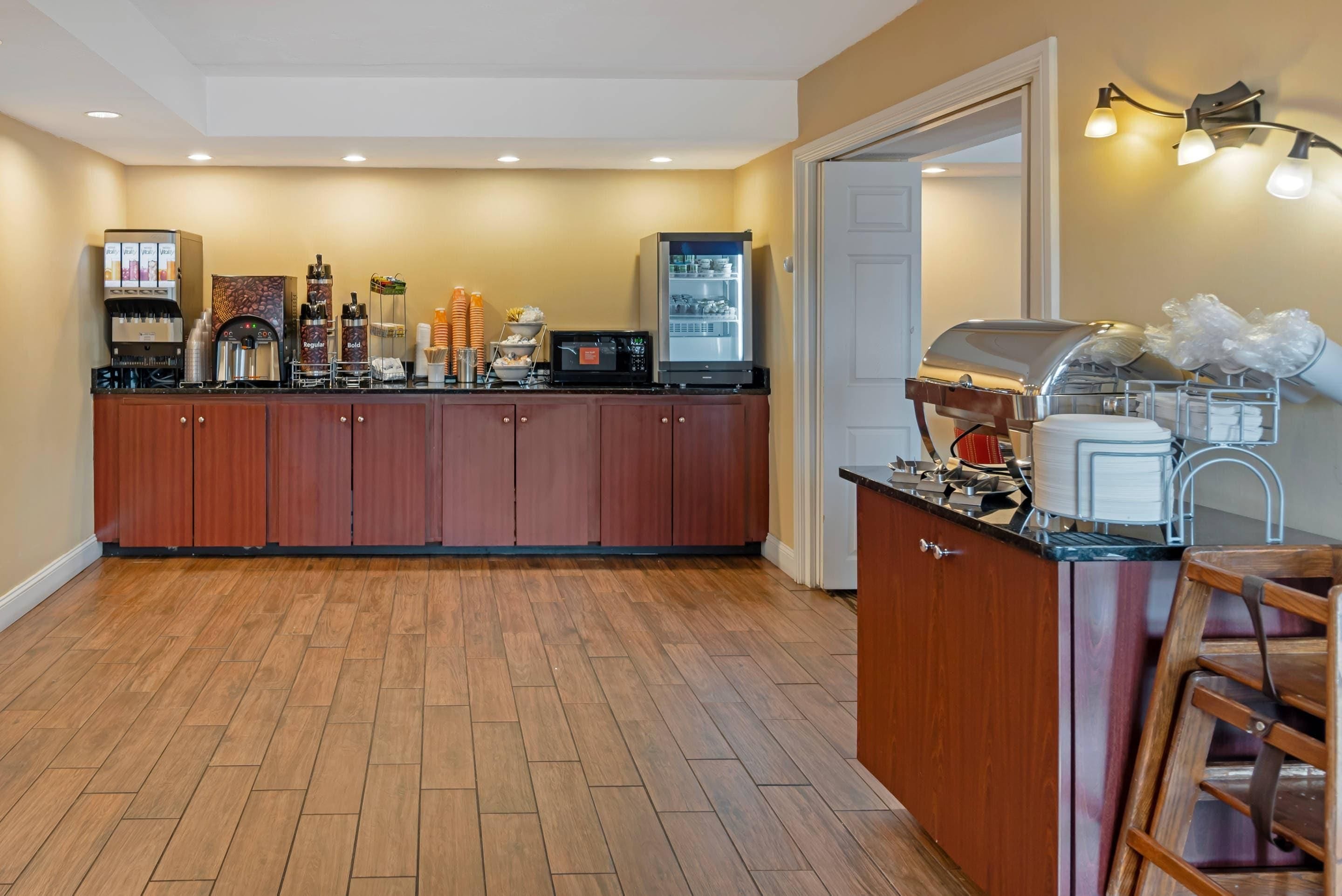 A kitchen with a coffee machine, microwave, refrigerator, and a grill.
