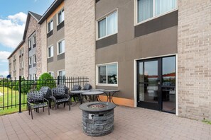 Un edificio con fachada de ladrillo, varias ventanas y un patio con mobiliario exterior y un hogar para la chimenea.