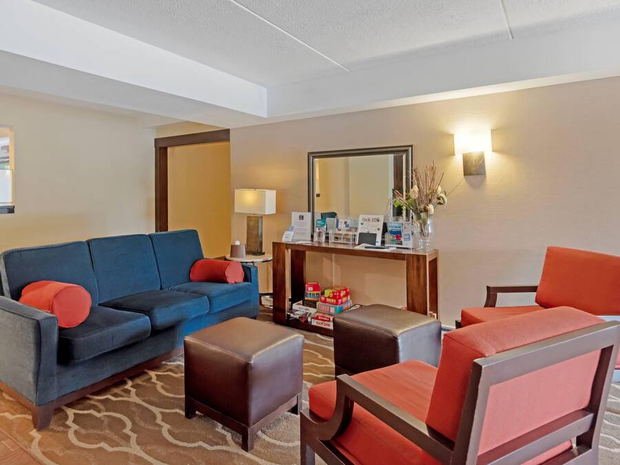A hotel lobby with a blue sofa, a red armchair, a small table, and a mirror on the wall.
