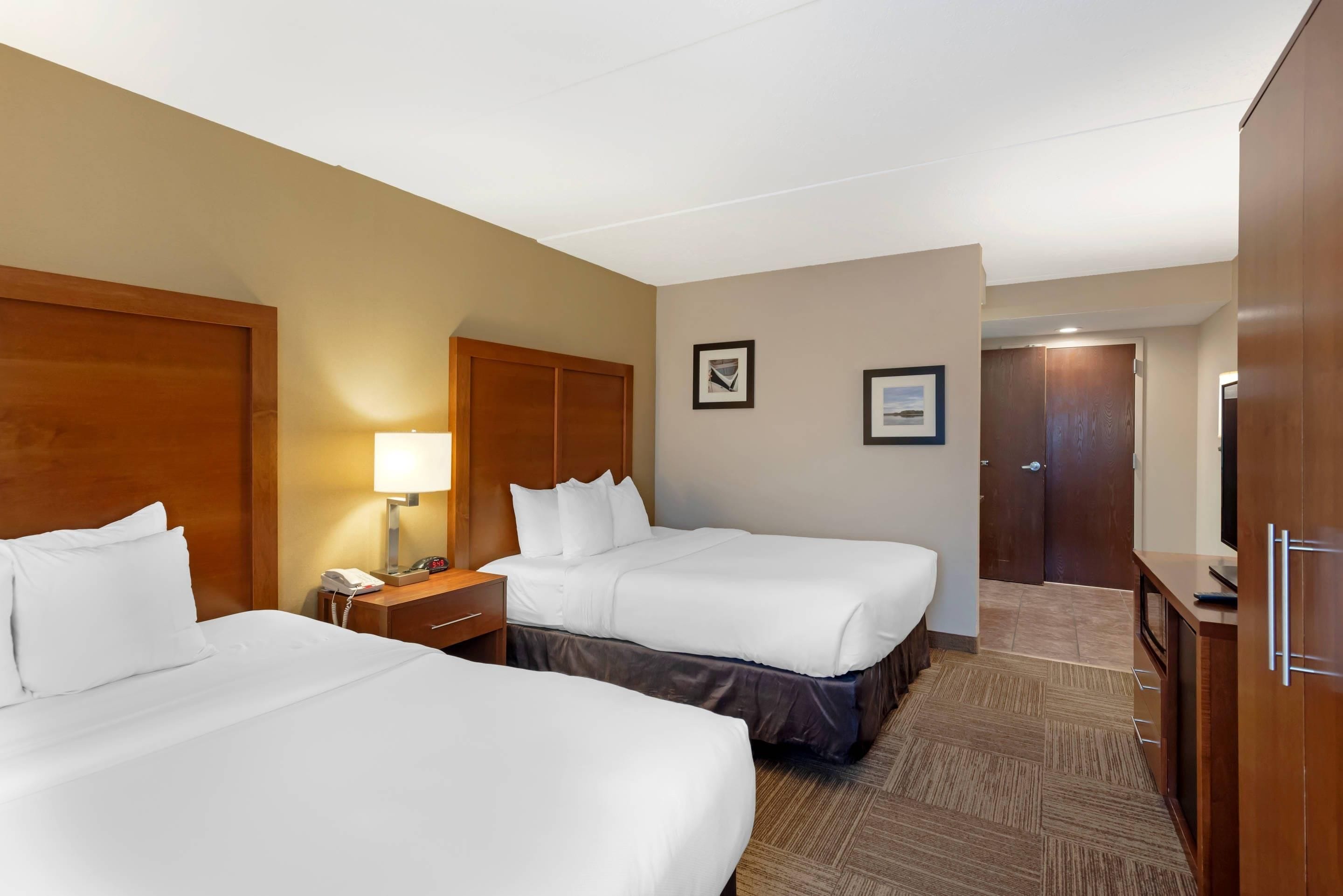 Une chambre d’hôtel avec deux lits, une table de chevet, une lampe, une horloge et une porte.