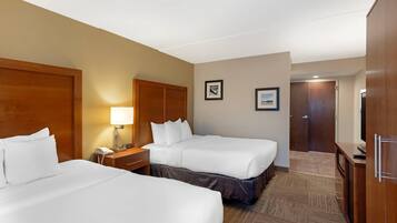 A hotel room with two beds, a nightstand, a lamp, a clock, and a door.