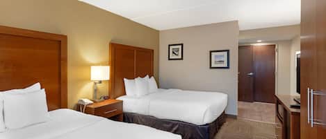 Une chambre d’hôtel avec deux lits, une table de chevet, une lampe, une horloge et une porte.