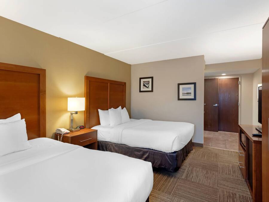 A hotel room with two beds, a nightstand, a lamp, a clock, and a door.