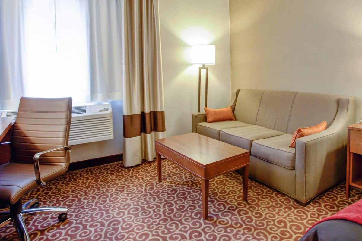 Une chambre d’hôtel avec un canapé, une petite table, une chaise, une lampe et une fenêtre avec des rideaux.