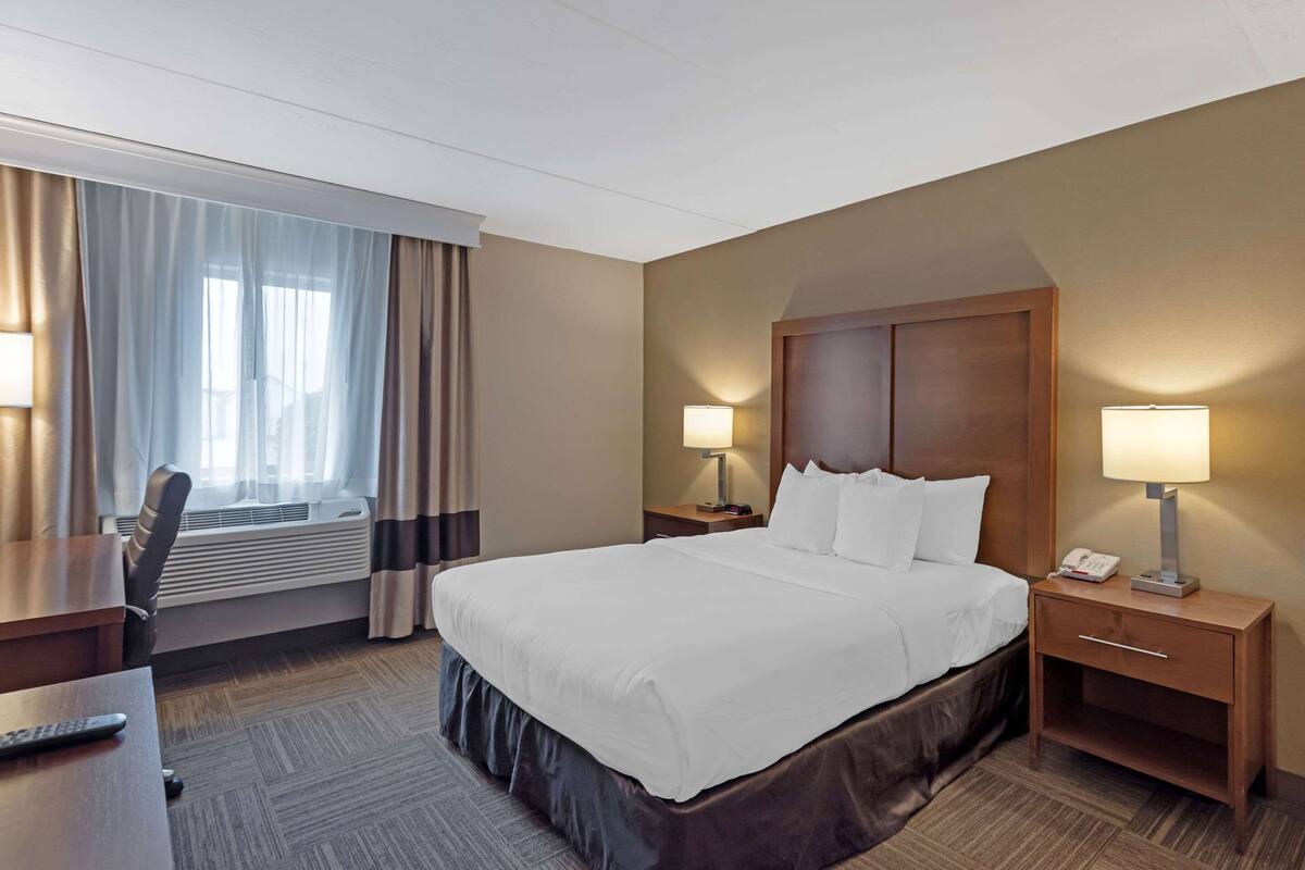 Une chambre d’hôtel avec un grand lit, deux tables de chevet avec des lampes, un bureau avec une chaise et une fenêtre avec des rideaux.