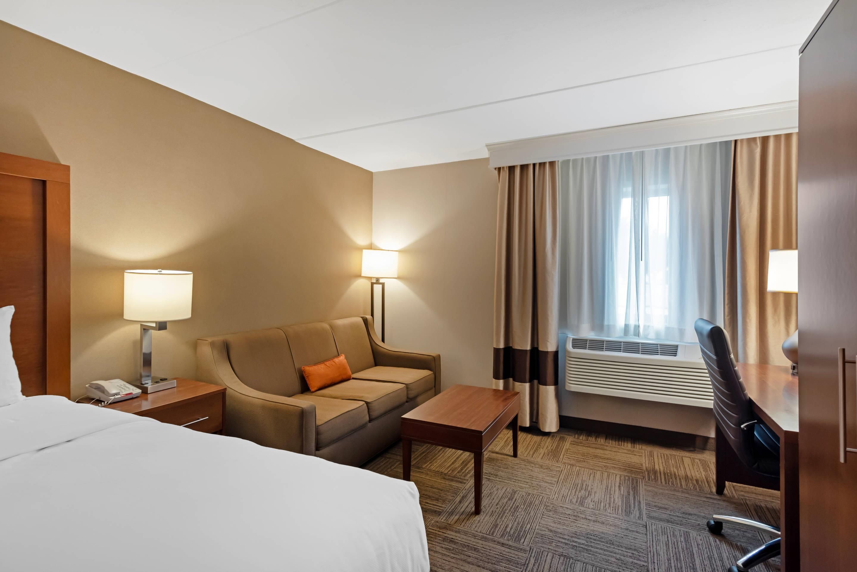 A hotel room with a bed, a sofa, a desk, a chair, a telephone, and a window with curtains.