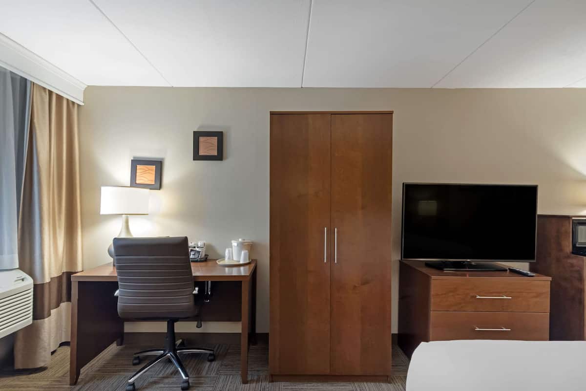 Une chambre d’hôtel équipée d’un lit, d’un bureau avec une lampe, d’une télévision, d’une armoire et d’une machine à café.
