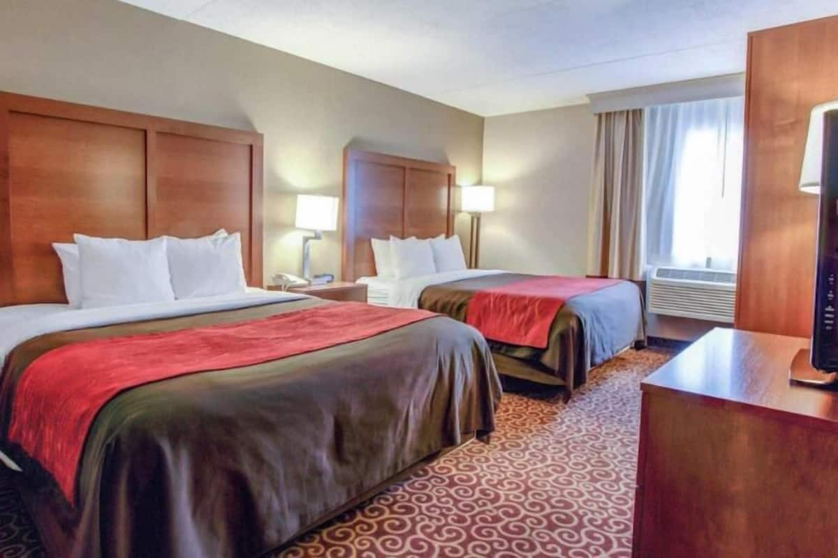 Une chambre d’hôtel avec deux lits, un bureau, une lampe et une fenêtre avec des rideaux.