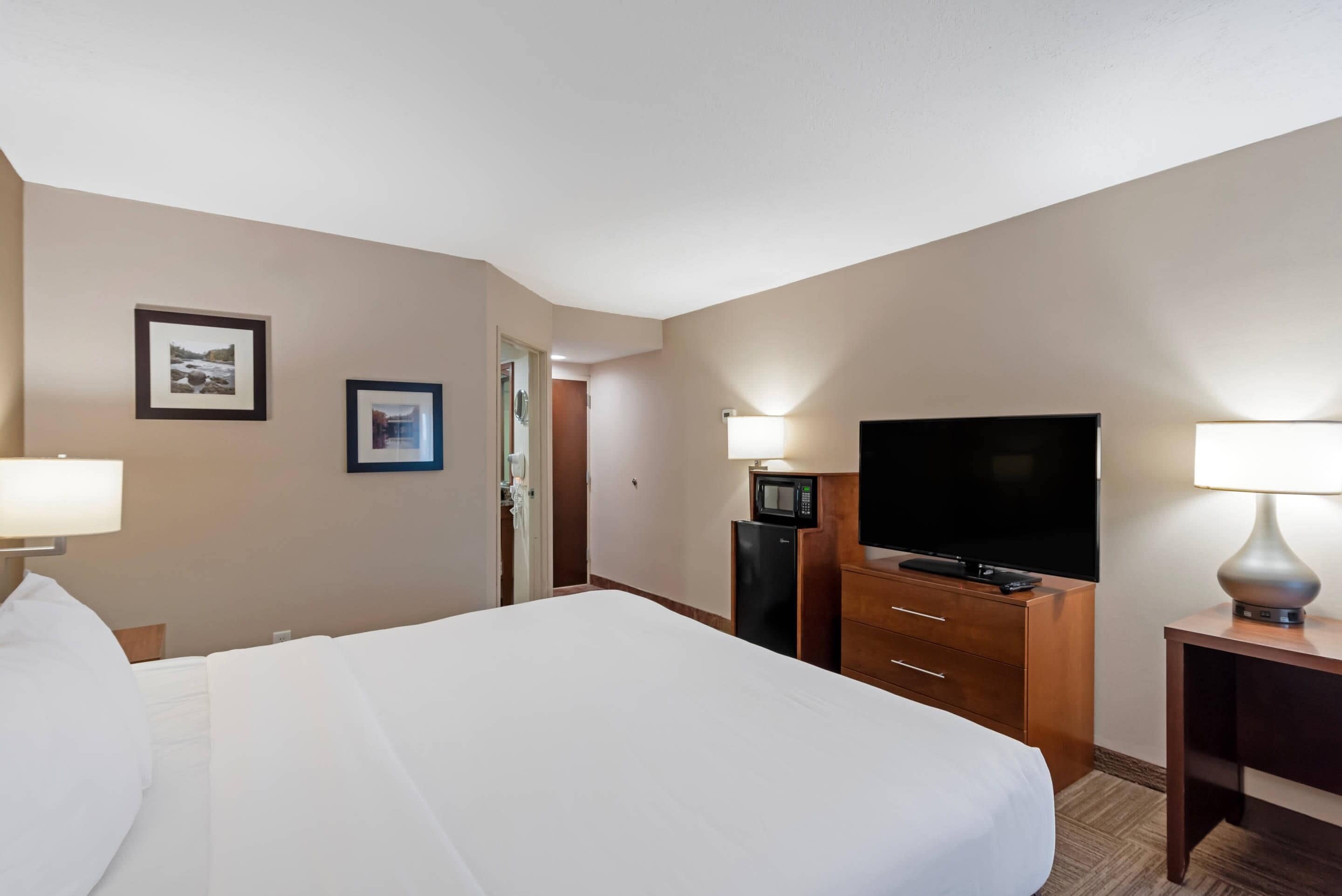 A hotel room with a bed, a flat-screen TV, a minibar, and two wall-mounted lamps.
