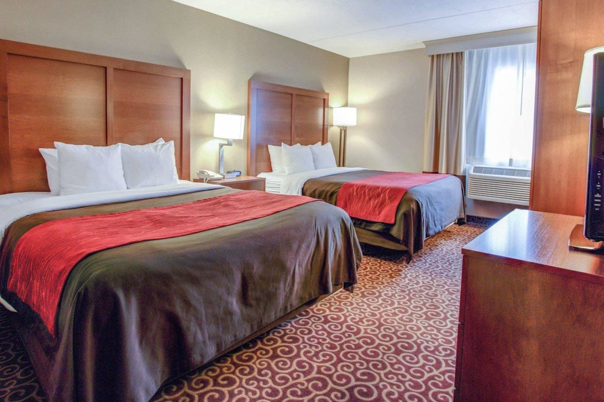 Une chambre d’hôtel avec deux lits, un bureau, une lampe, un climatiseur et une fenêtre avec des rideaux.