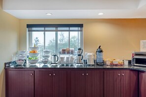 A modern kitchen with a large window, equipped with coffee makers, a toaster, and various food items.