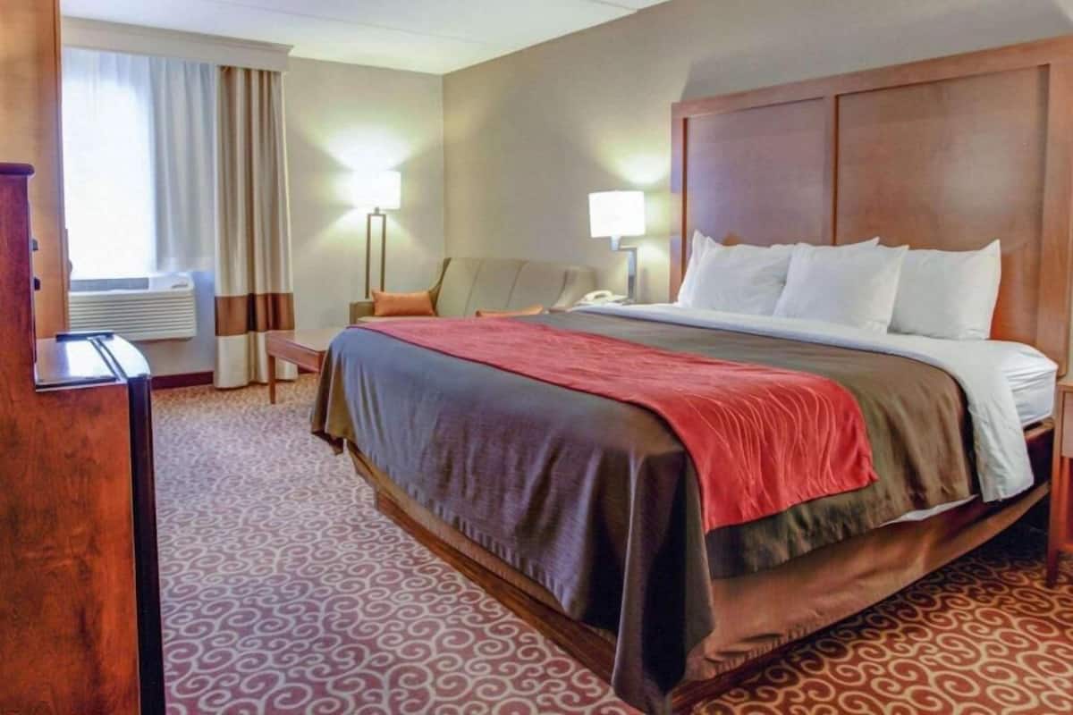Une chambre d’hôtel avec un grand lit, un bureau, une chaise, une lampe et une fenêtre avec des rideaux.