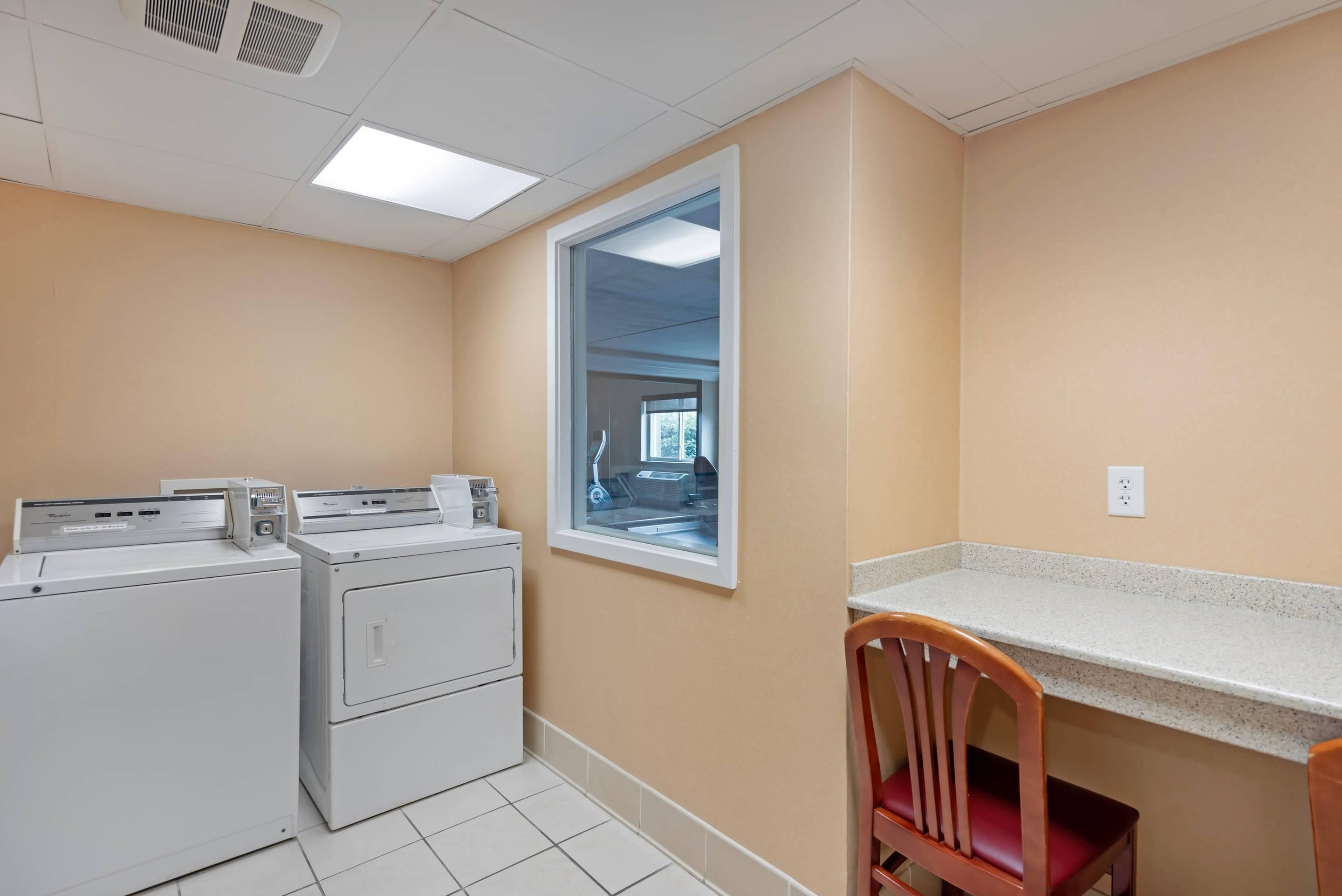 A laundry room with stacked washers and dryers, a window, and a countertop with a chair.