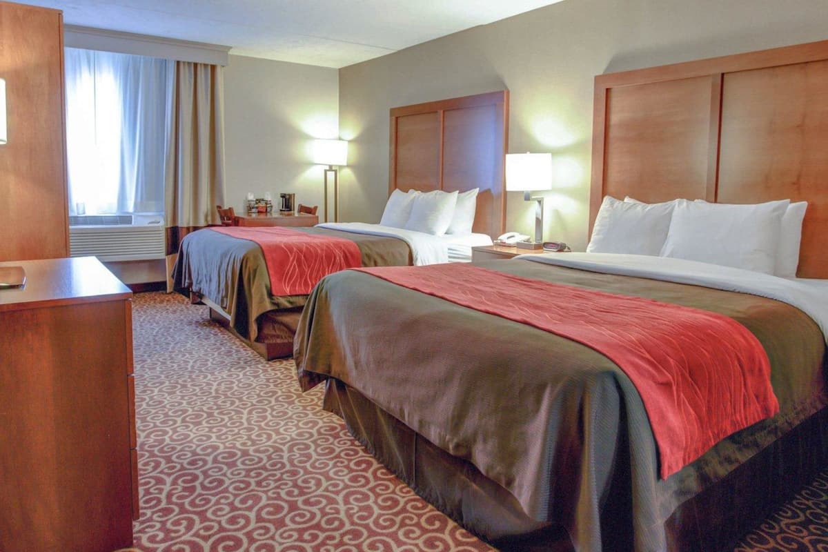 Une chambre d’hôtel avec deux lits, un bureau, une chaise, une lampe et une fenêtre avec des rideaux.