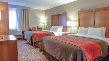 A hotel room with two beds, a desk, a chair, a lamp, and a window with curtains.