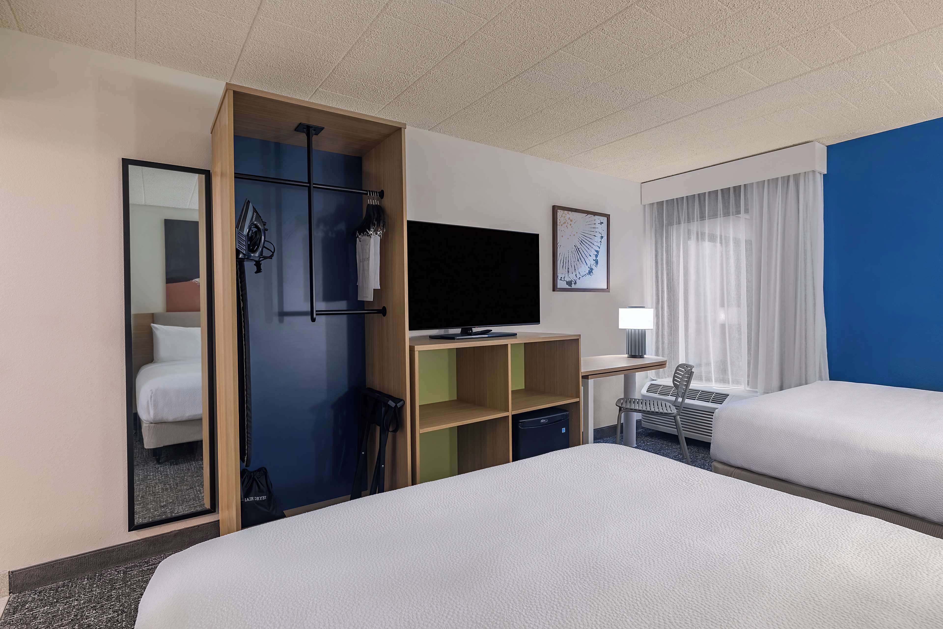 Hotellihuone, jossa on kaksi sänkyä, televisio, työpöytä ja tuoli.