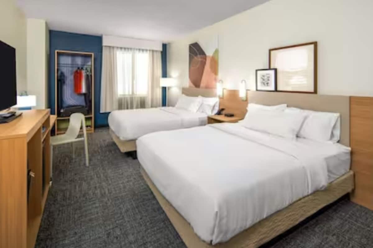 Une chambre d’hôtel avec deux lits, un bureau, une chaise, une armoire et une fenêtre avec des rideaux.