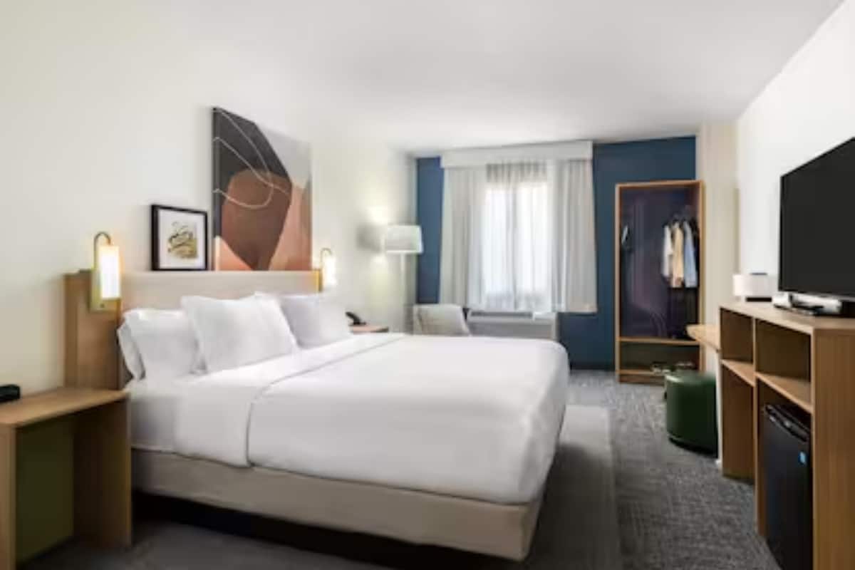 Une chambre d’hôtel comprenant un lit, des tables de chevet, une télévision, une armoire et une fenêtre avec des rideaux.