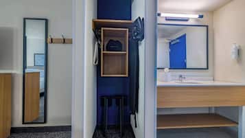 A hotel bathroom with a mirror, sink, and storage shelves.