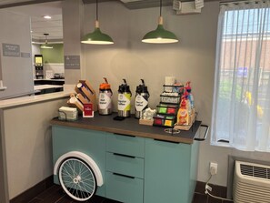 A cafe counter with a coffee machine, water dispenser, and decaf coffee machine. There are also condiments and a menu on the counter.