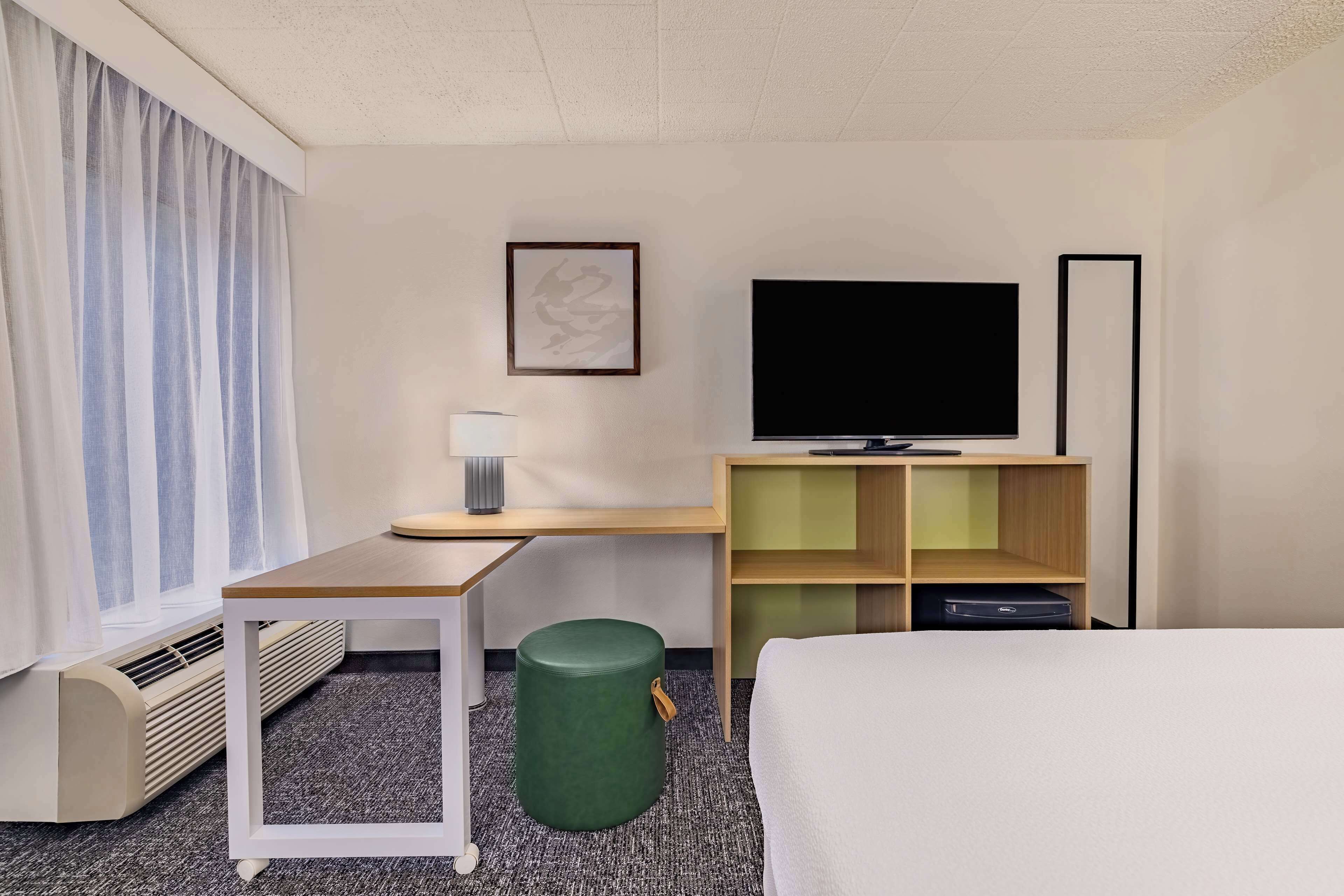 A hotel room with a bed, a desk, a television, a lamp, a waste bin, and a radiator.