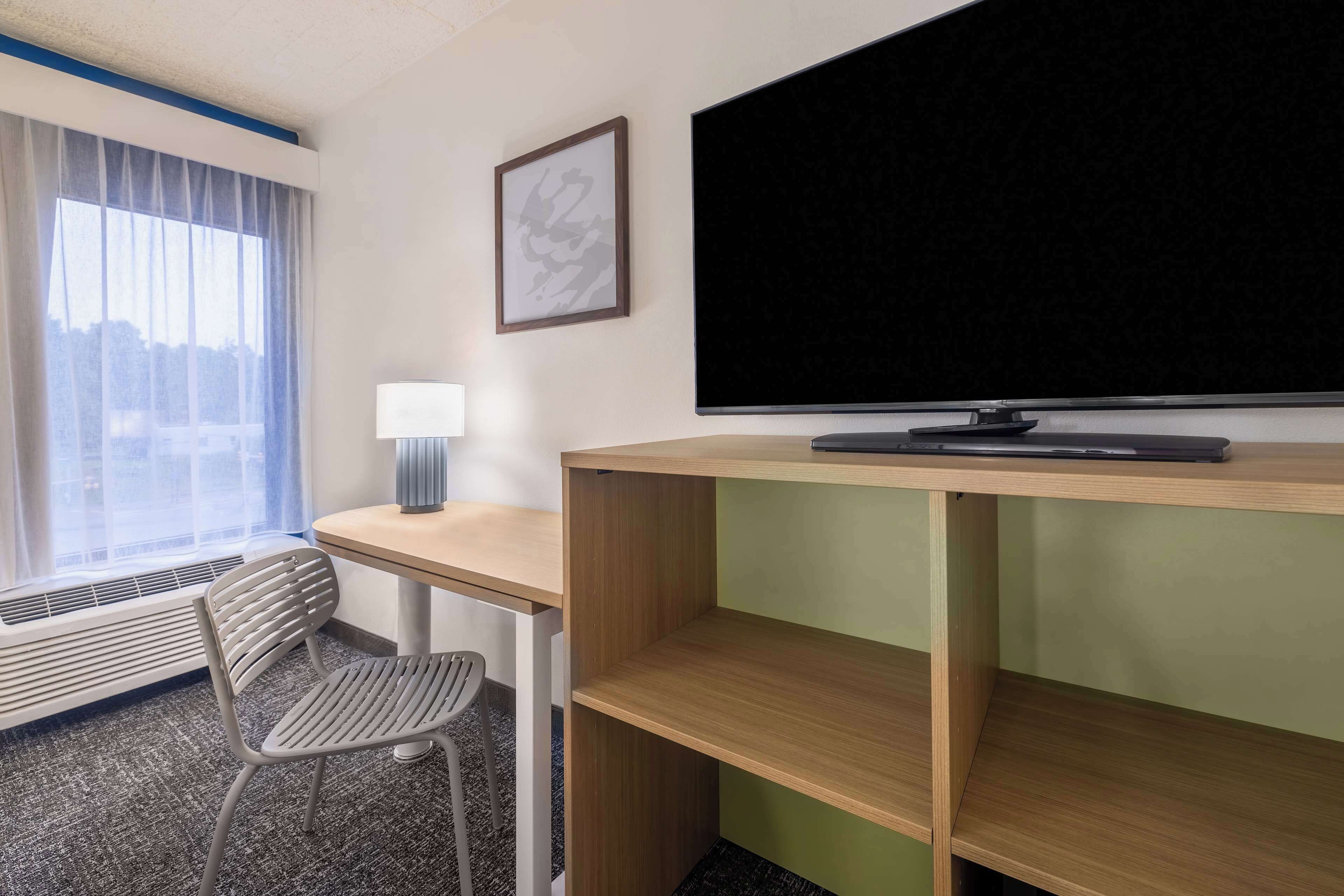 A hotel room with a desk, chair, television, and a window with curtains.