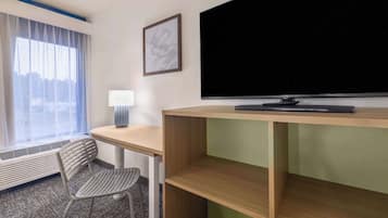 Une chambre d’hôtel équipée d’un bureau, d’une chaise, d’une télévision et d’une fenêtre avec des rideaux.