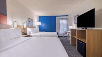 A hotel room with two beds, a desk with a television, a chair, and a small refrigerator.