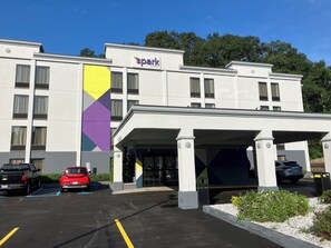 A hotel with a modern design, featuring a prominent 'spark by Hilton' sign, a covered entrance, and a parking area with several vehicles.