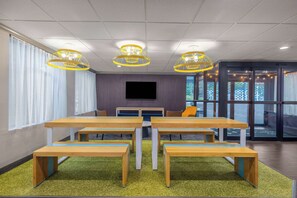 A conference room with a large screen, wooden tables, benches, and yellow pendant lights.
