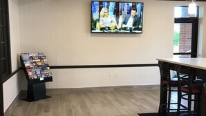 A spacious lobby with a flat-screen TV displaying a news program, a magazine rack, and a bar area with stools. - Travelodge by Wyndham Canton/Livonia Area, MI (Canton)