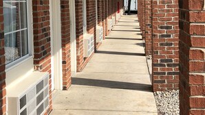 A long corridor with brick walls and white-framed windows, leading to a covered area with a row of air conditioning units. - Travelodge by Wyndham Canton/Livonia Area, MI (Canton)