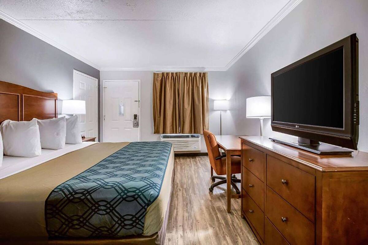 A hotel room with a bed, a desk, a television, a dresser, and a window with curtains.