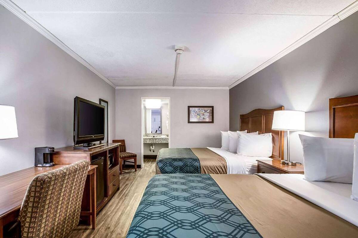 A hotel room with two beds, a desk with a television, a chair, and a bathroom visible through an open door.