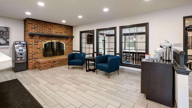 A modern lobby with a brick fireplace, seating area, and large windows. - Travelodge by Wyndham Canton/Livonia Area, MI (Canton)