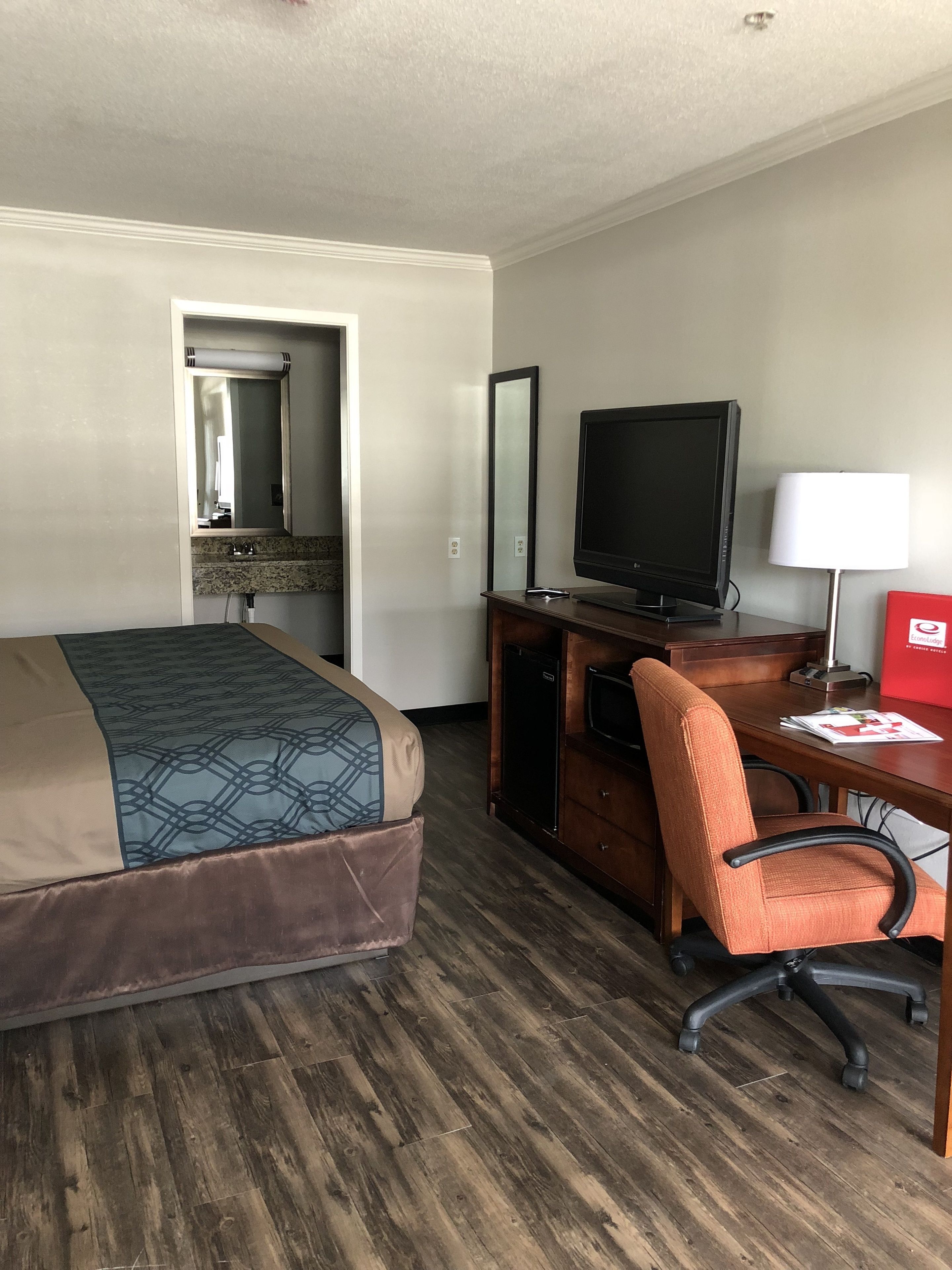 A hotel room with a bed, a desk with a chair, a television, and a mirror.