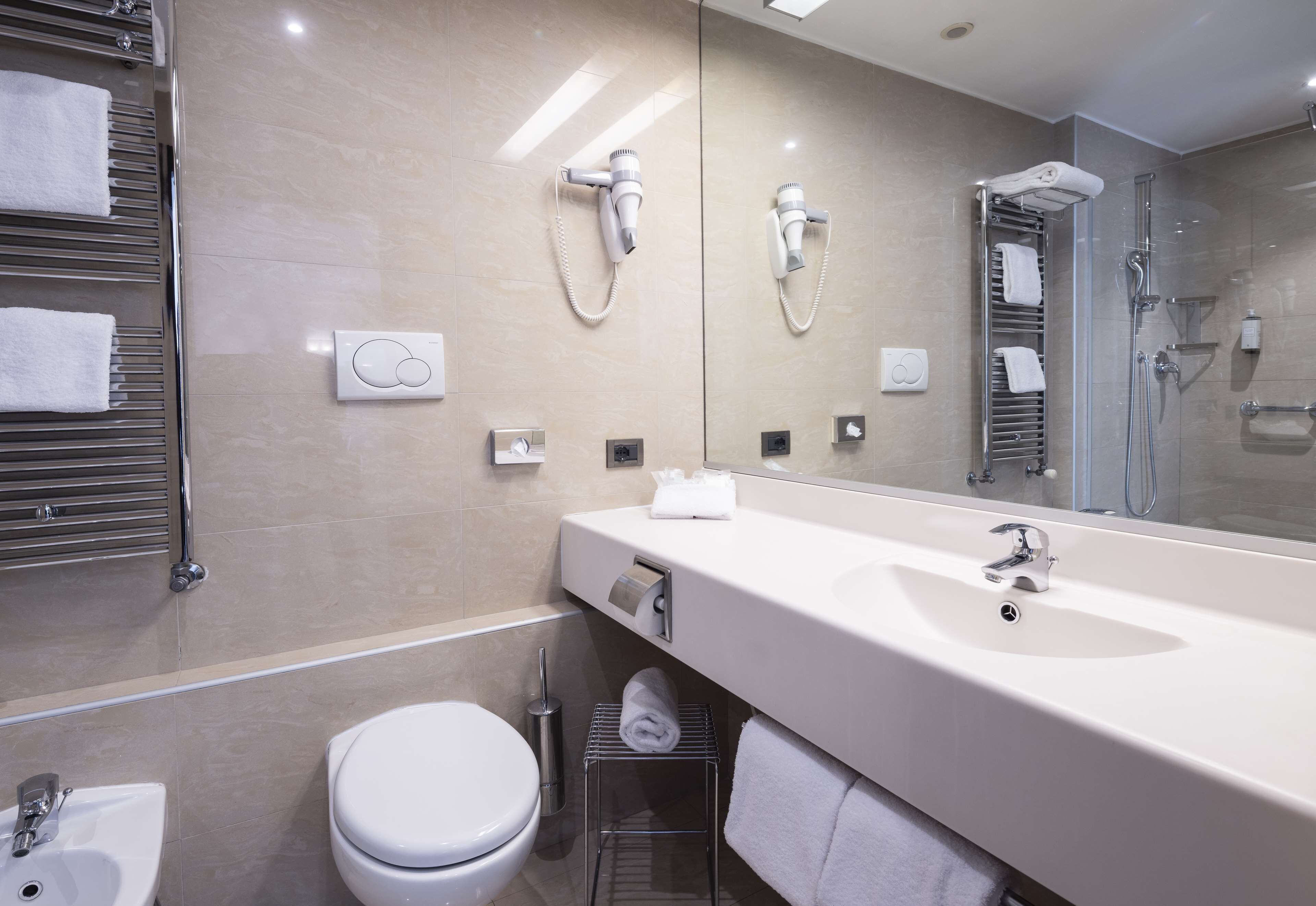 Un bagno moderno con uno specchio grande, un lavandino, un water e una zona doccia.