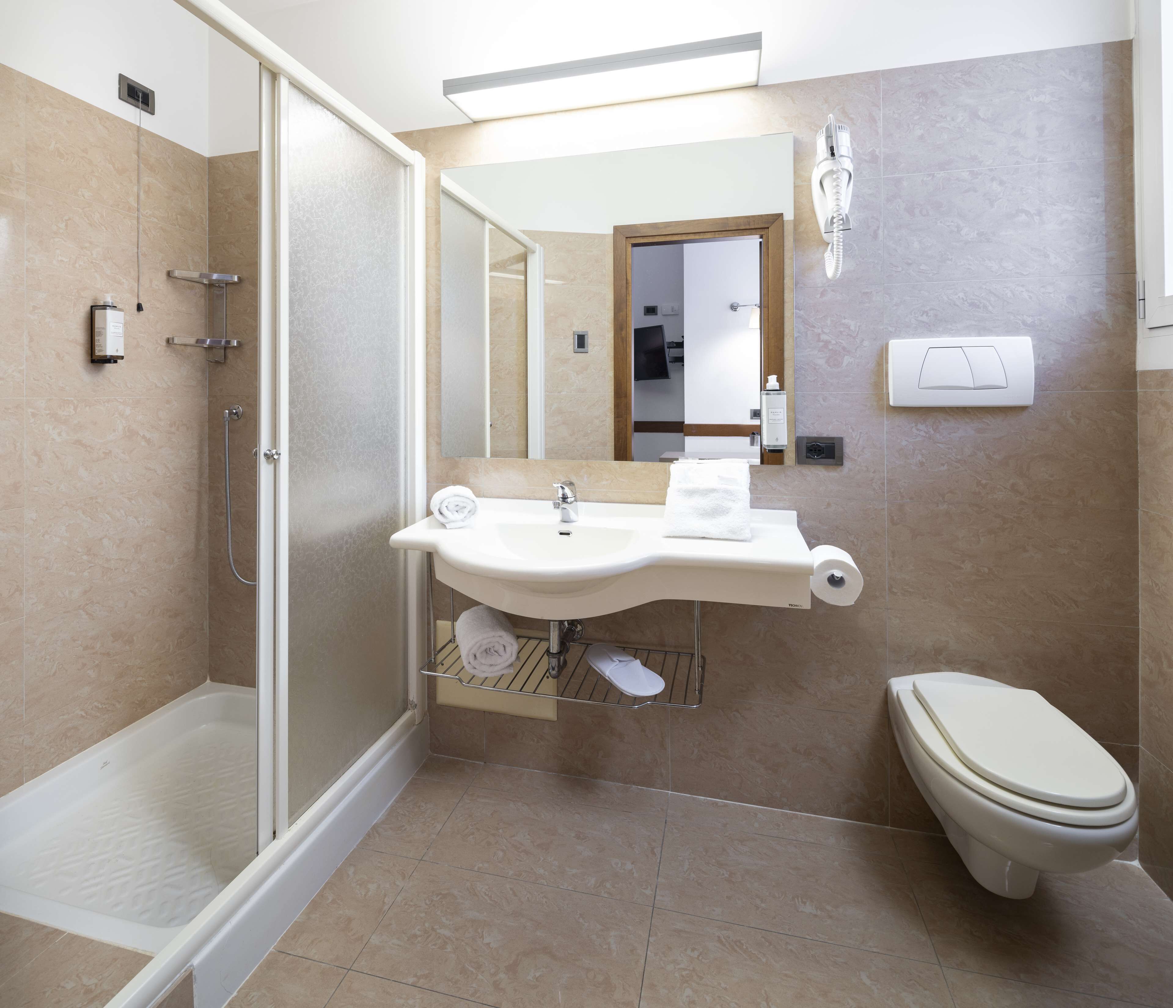Et moderne badeværelse med en glasafskærmet brusekabine, en vask med håndklæderadiator og et toilet.