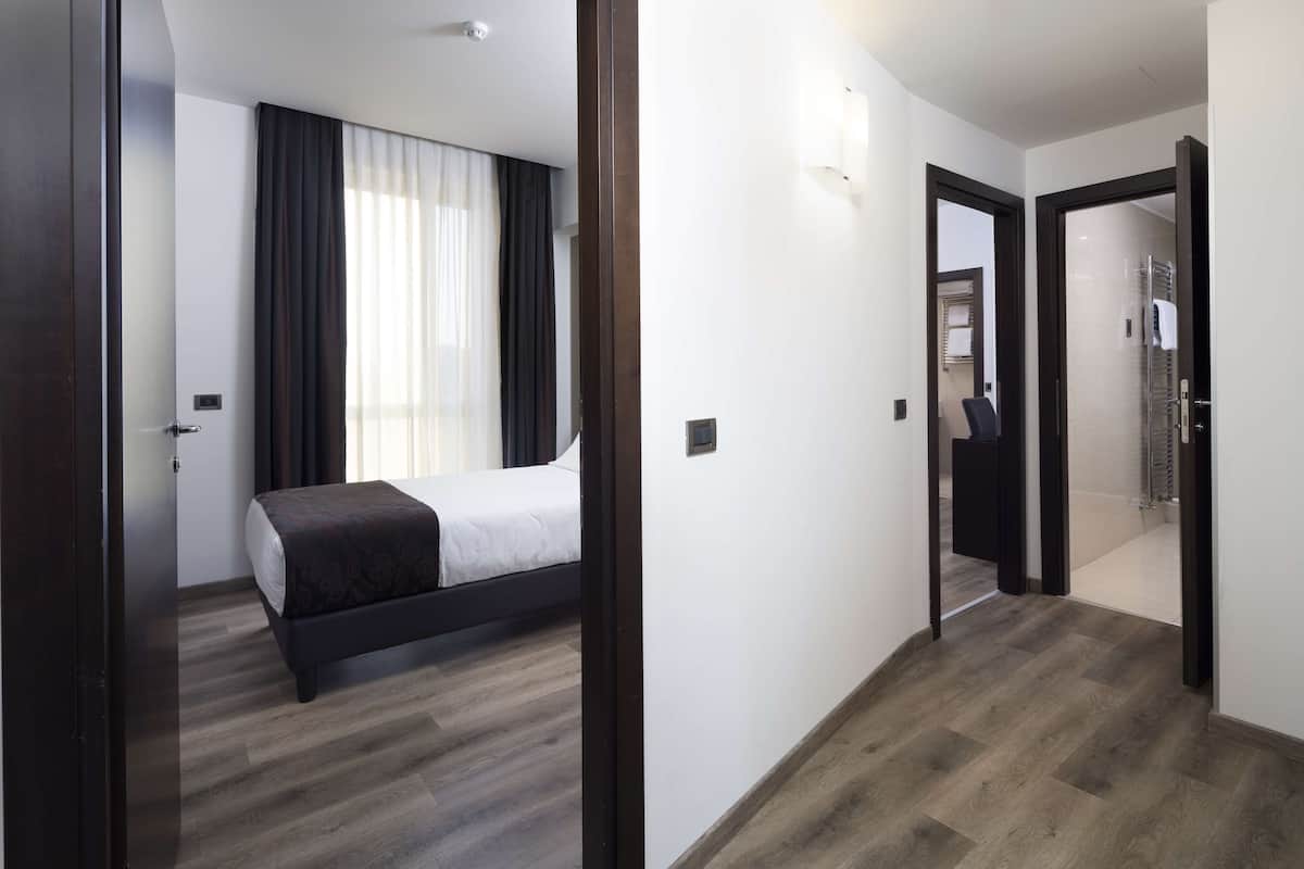 Une chambre d’hôtel avec un lit, un miroir, une porte et un couloir.