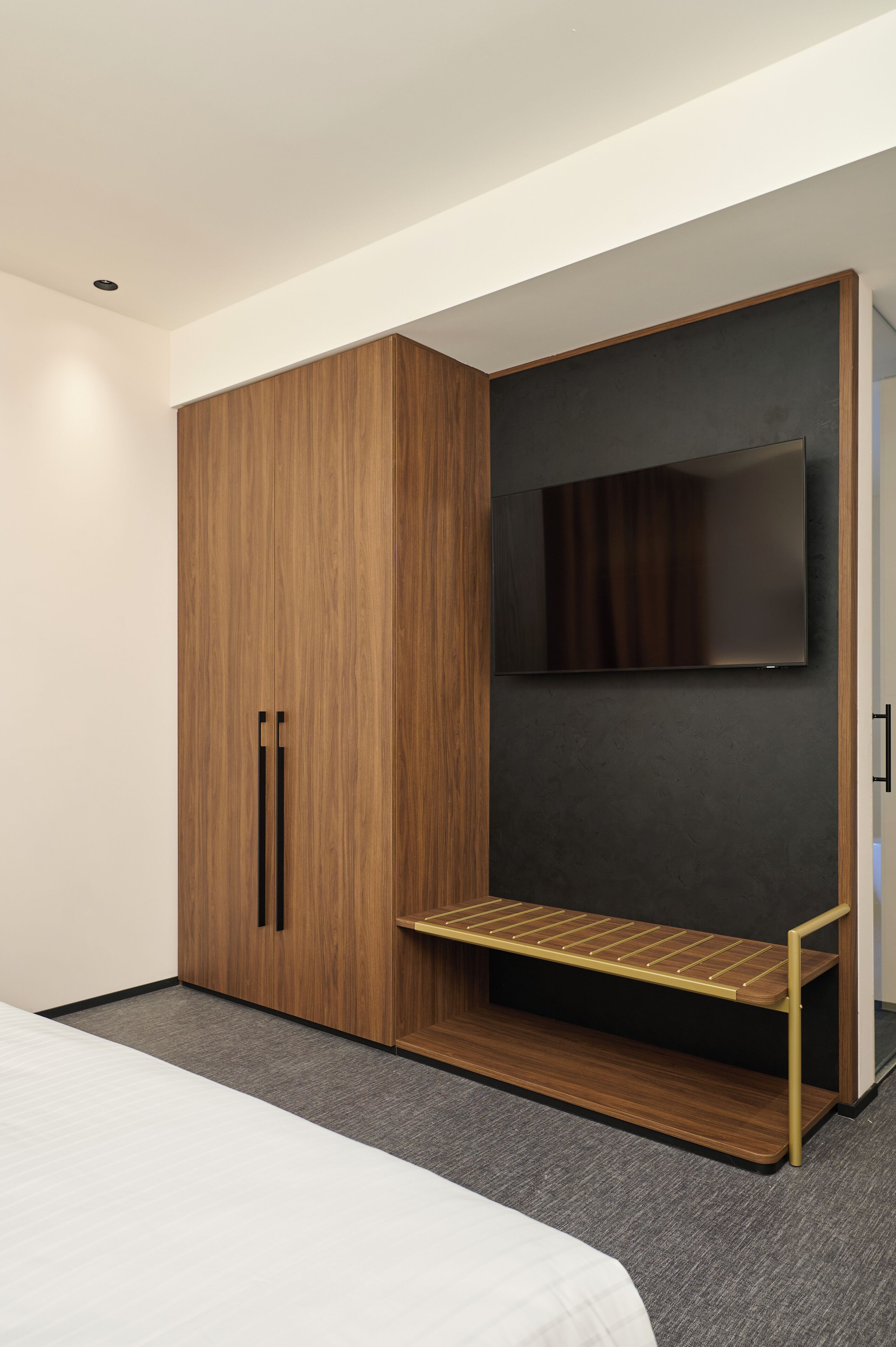 A bedroom with a bed, a wardrobe, a bench, and a television.