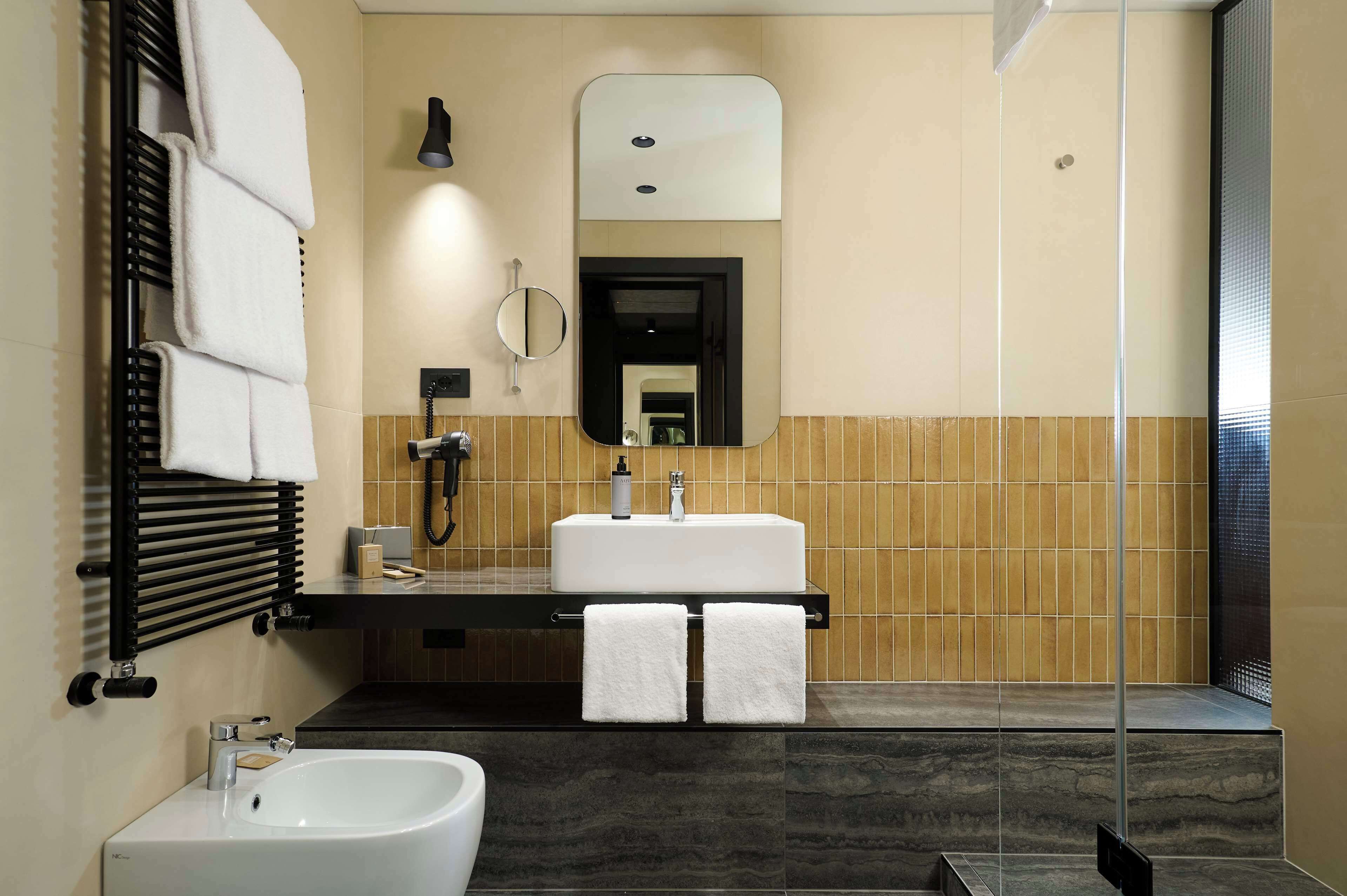 Een moderne badkamer met een zwarte handdoekhouder, een witte wastafel, een bidet en een spiegel.