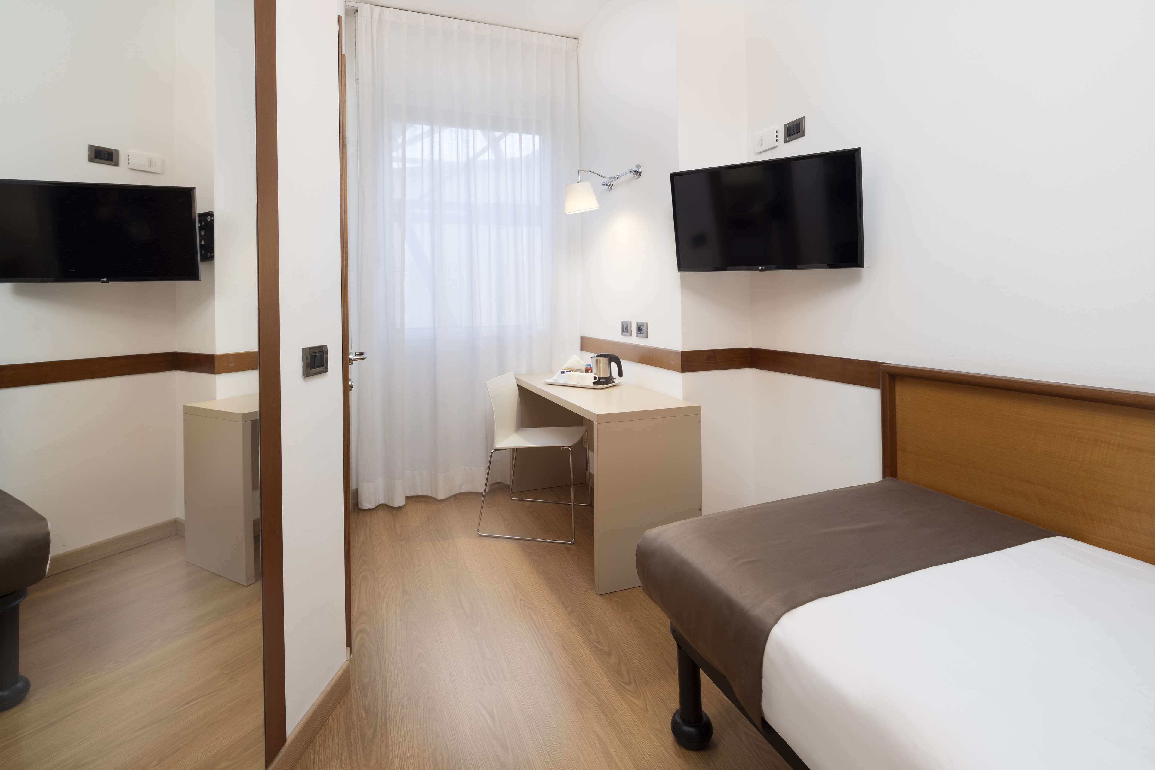 Ein Hotelzimmer mit Bett, Schreibtisch, Stuhl, Fernseher und einem Fenster mit Vorhängen.