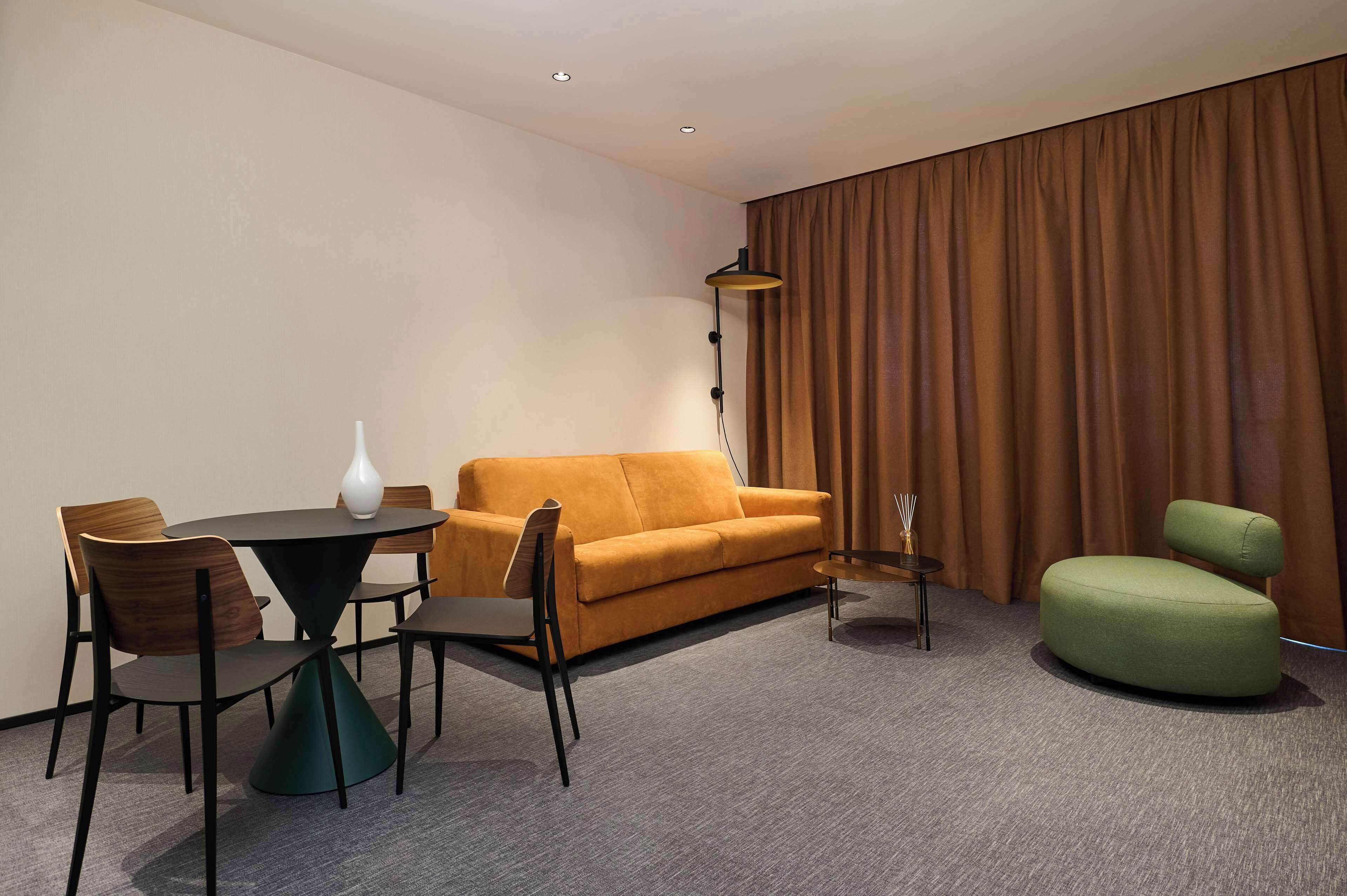 Una habitación de hotel moderna con una mesa redonda, dos sofás y un sillón verde.