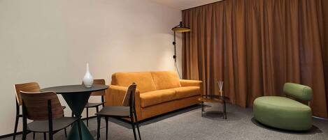 Una habitación de hotel moderna con una mesa redonda, dos sofás y un sillón verde.