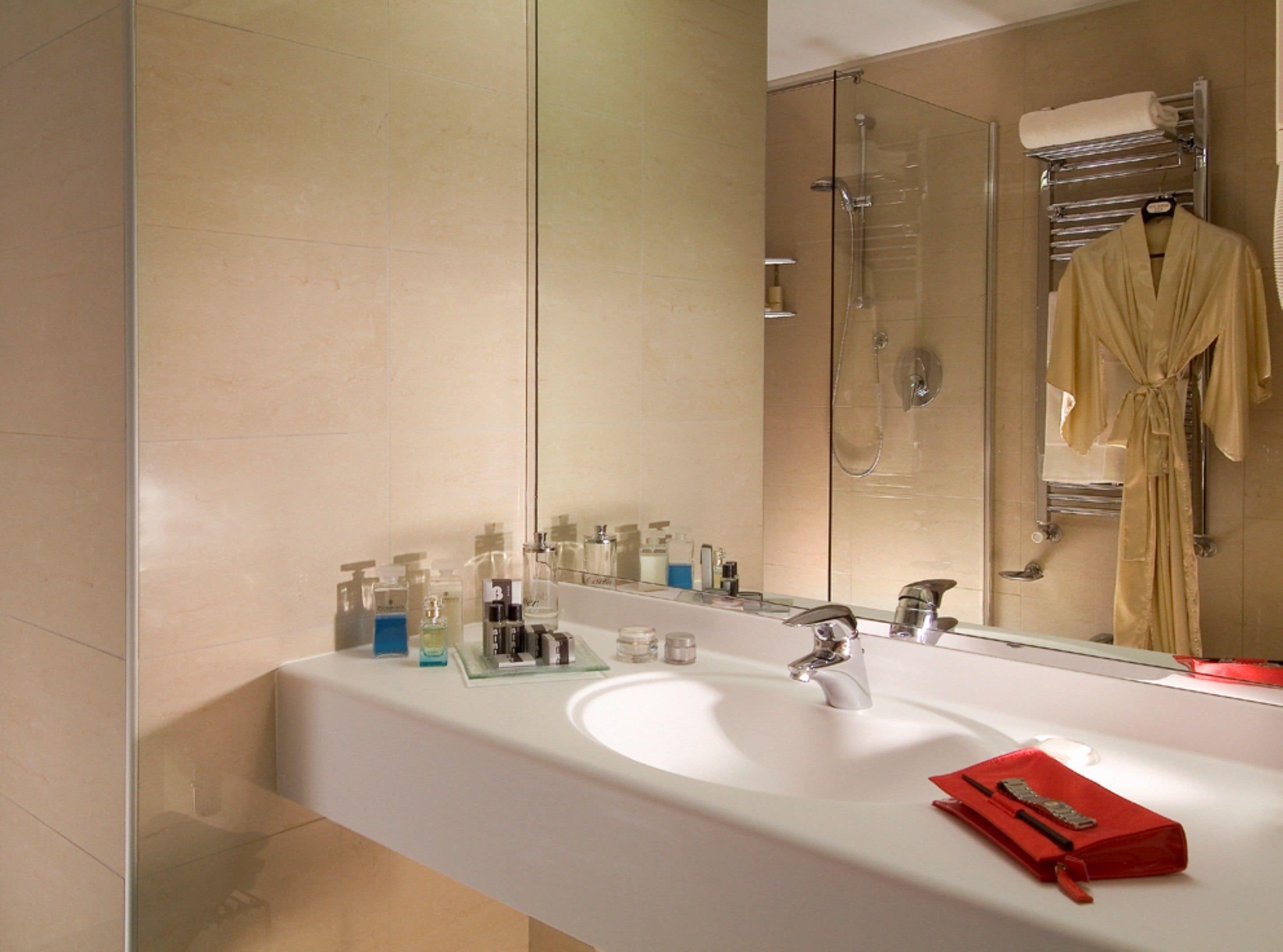 Une salle de bain moderne avec un grand miroir, un lavabo blanc et une cabine de douche en verre.