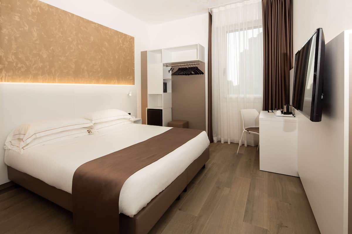 Une chambre d’hôtel moderne dotée d’un grand lit, d’un bureau avec un téléviseur à écran plat, d’une armoire et d’un dressing.