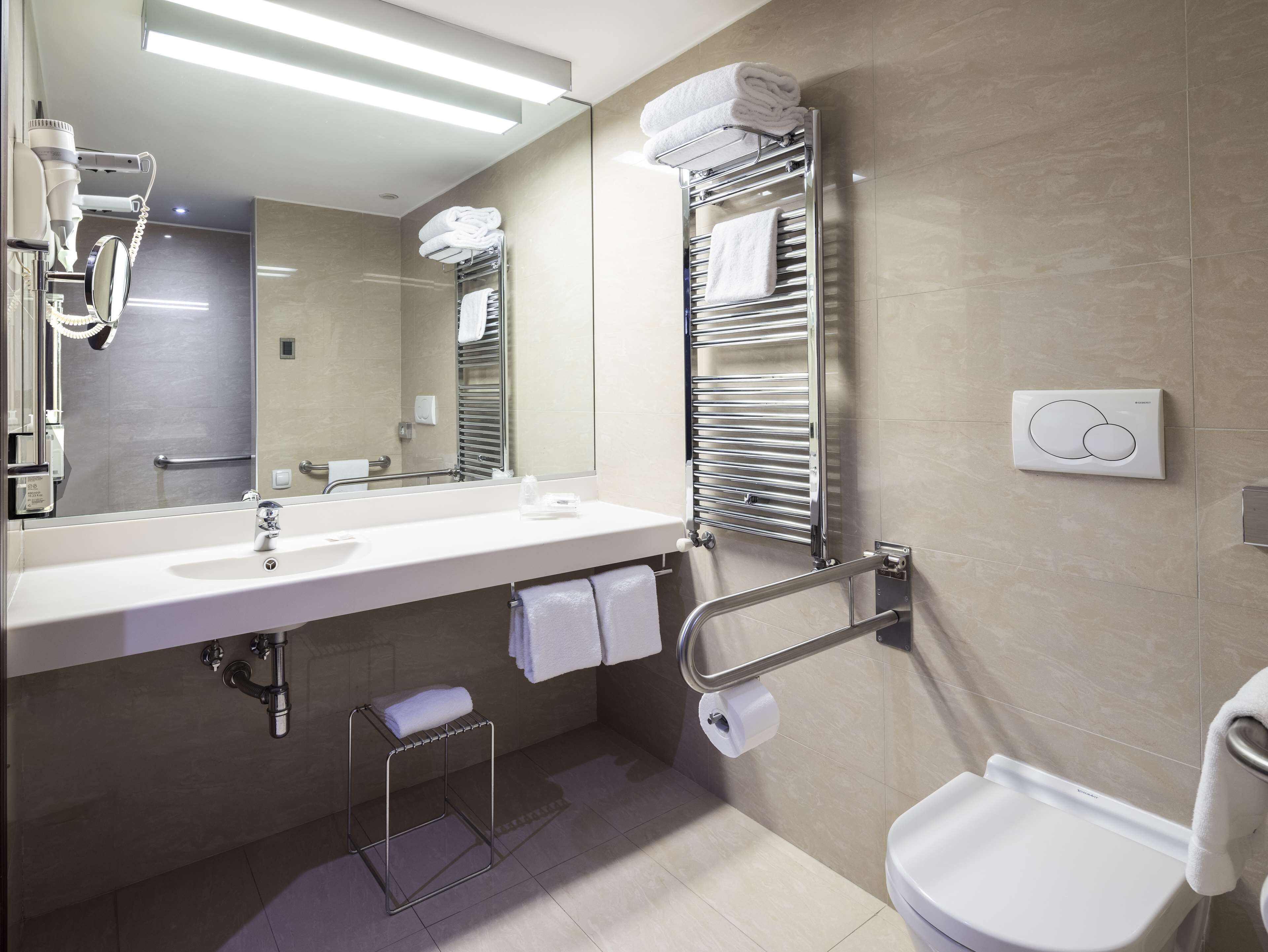 A modern bathroom with a large mirror, a sink, a toilet, and towel racks.